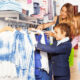 A woman and two children are shopping for clothes in a store. One child is wearing a suit jacket and the other is carrying a shopping bag.